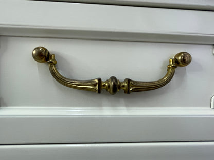 Close view of an original curved brass drawer handle with light natural patina
