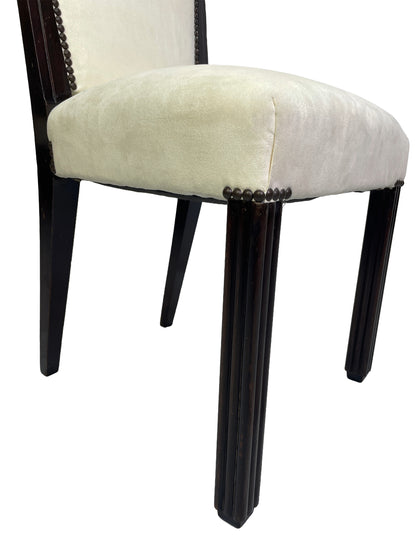 Close-up detail of a vintage Art Deco style side chair showing ivory suede-like upholstery, nailhead trim, and fluted dark wood legs.