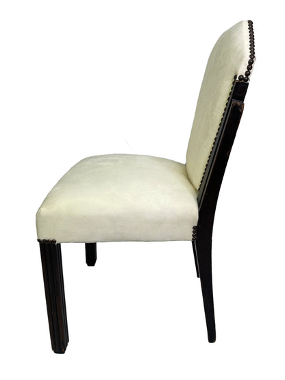 Side profile view of a vintage Art Deco style dining chair with ivory suede-like upholstery, nailhead trim, and dark mahogany legs.
