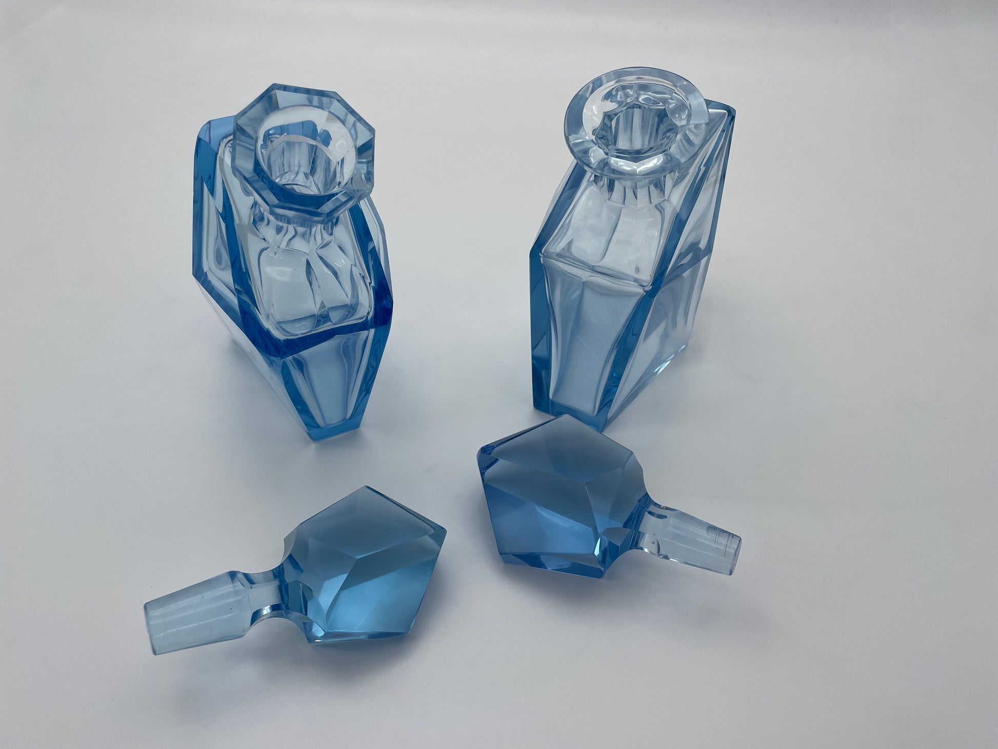Top view of a pair of vintage blue glass decanters with removable faceted stoppers displayed separately.