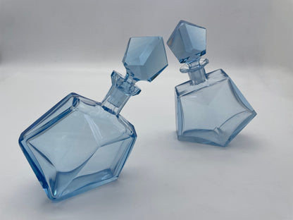 Vintage geometric blue glass decanters with matching faceted stoppers styled as decorative barware from a three-quarter angle.