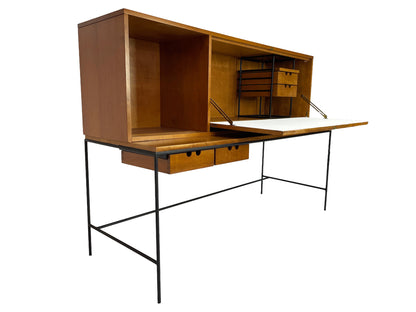Three-quarter view of a Paul McCobb Planner Group secretary desk in solid maple with black iron base and fold-down work surface, American mid-century modern design, 1950s.