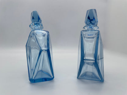 Side profile view of a pair of vintage blue glass decanters with sculptural geometric bodies and matching stoppers.