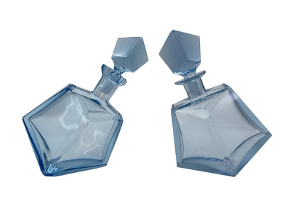 Pair of vintage sculptural blue glass decanters with matching faceted stoppers shown from an angled front view and white background.