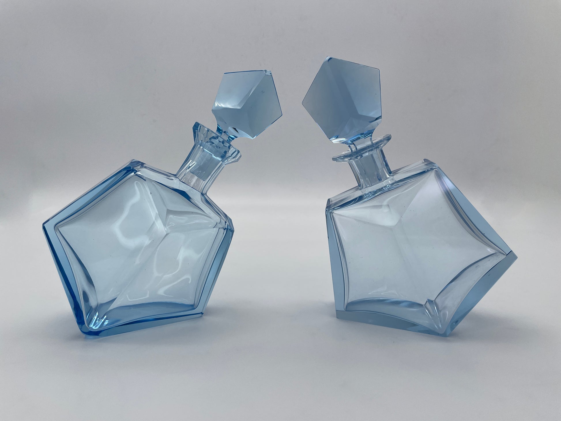 Pair of vintage sculptural blue glass decanters with matching faceted stoppers shown from an angled front view.