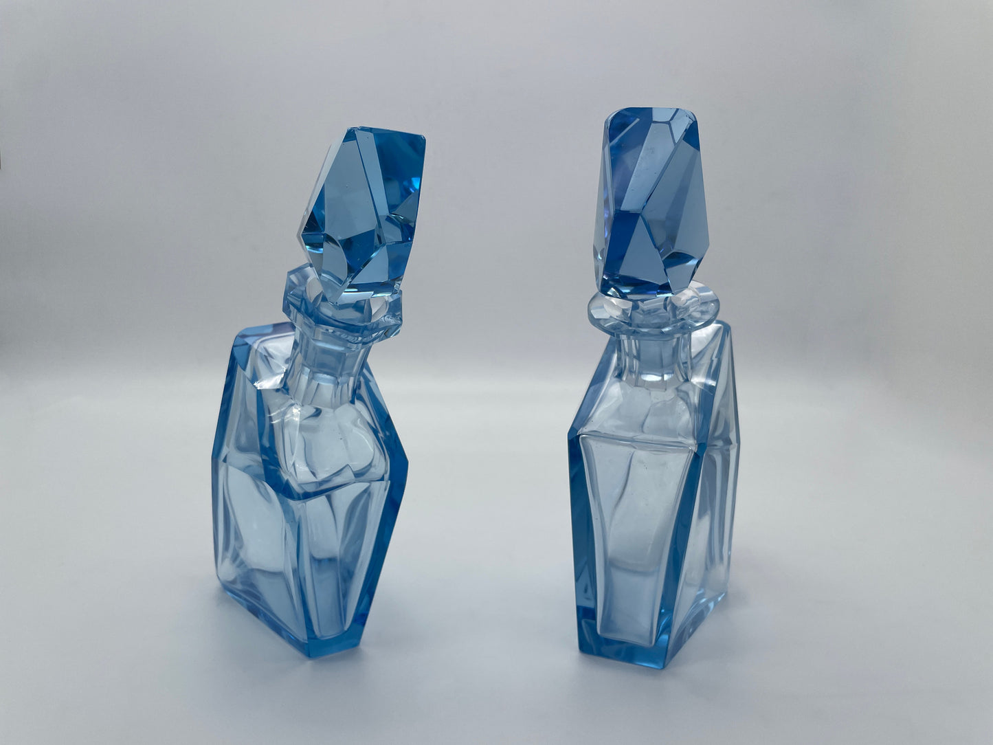 Upright view of a pair of sculptural vintage blue glass decanters with matching faceted stoppers.