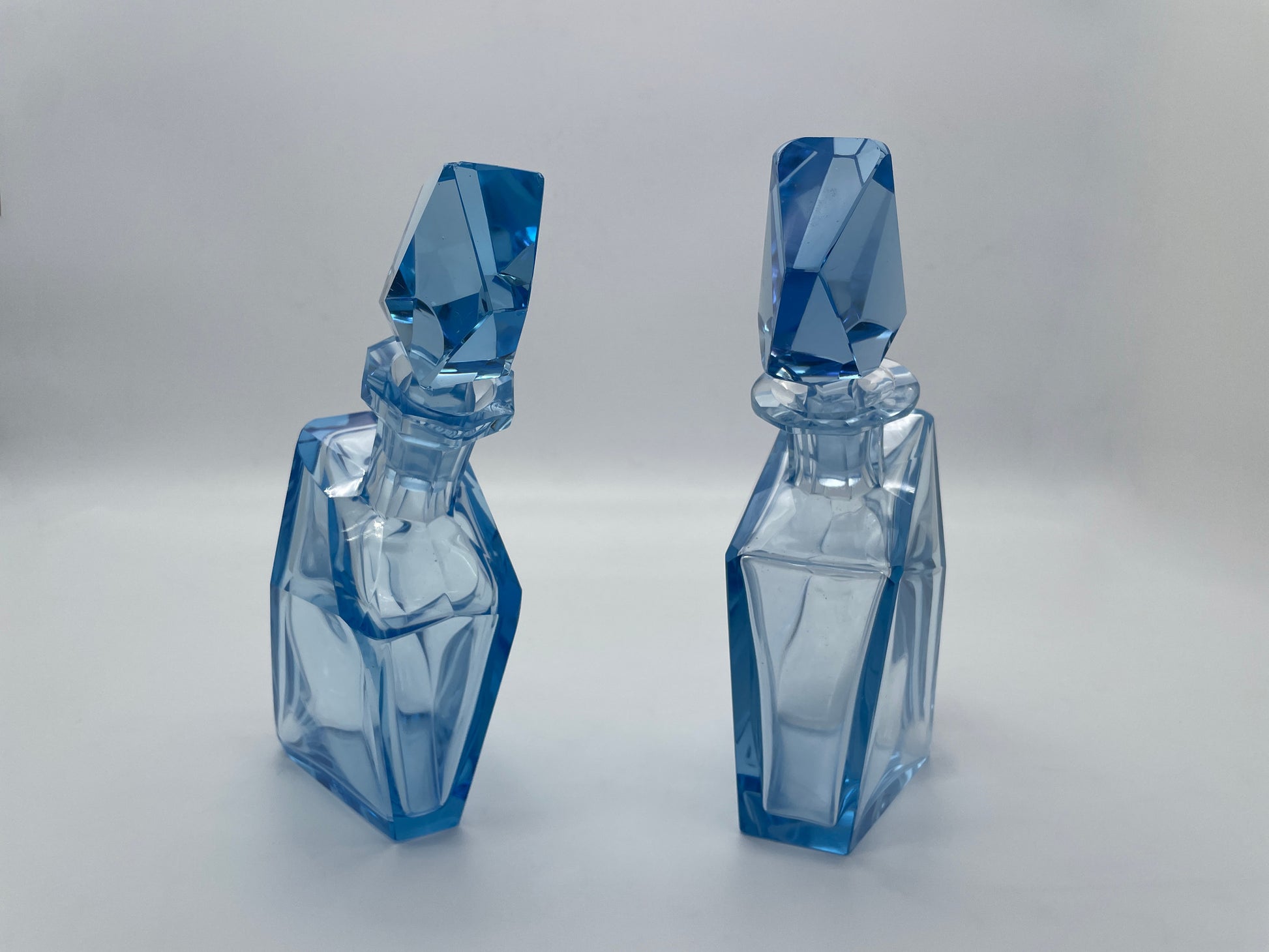 Upright view of a pair of sculptural vintage blue glass decanters with matching faceted stoppers.
