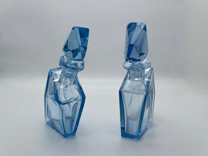Upright view of a pair of sculptural vintage blue glass decanters with matching faceted stoppers.