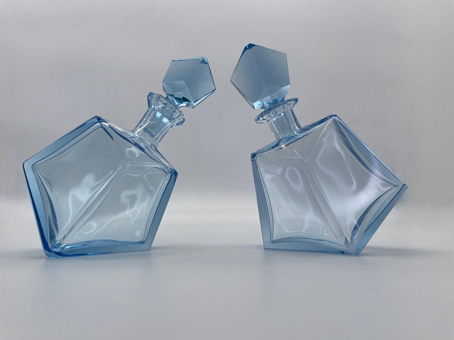 Pair of vintage blue glass decanters with matching faceted stoppers displayed together, featuring sculptural geometric forms.