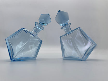 Pair of vintage blue glass decanters with matching faceted stoppers displayed together, featuring sculptural geometric forms.