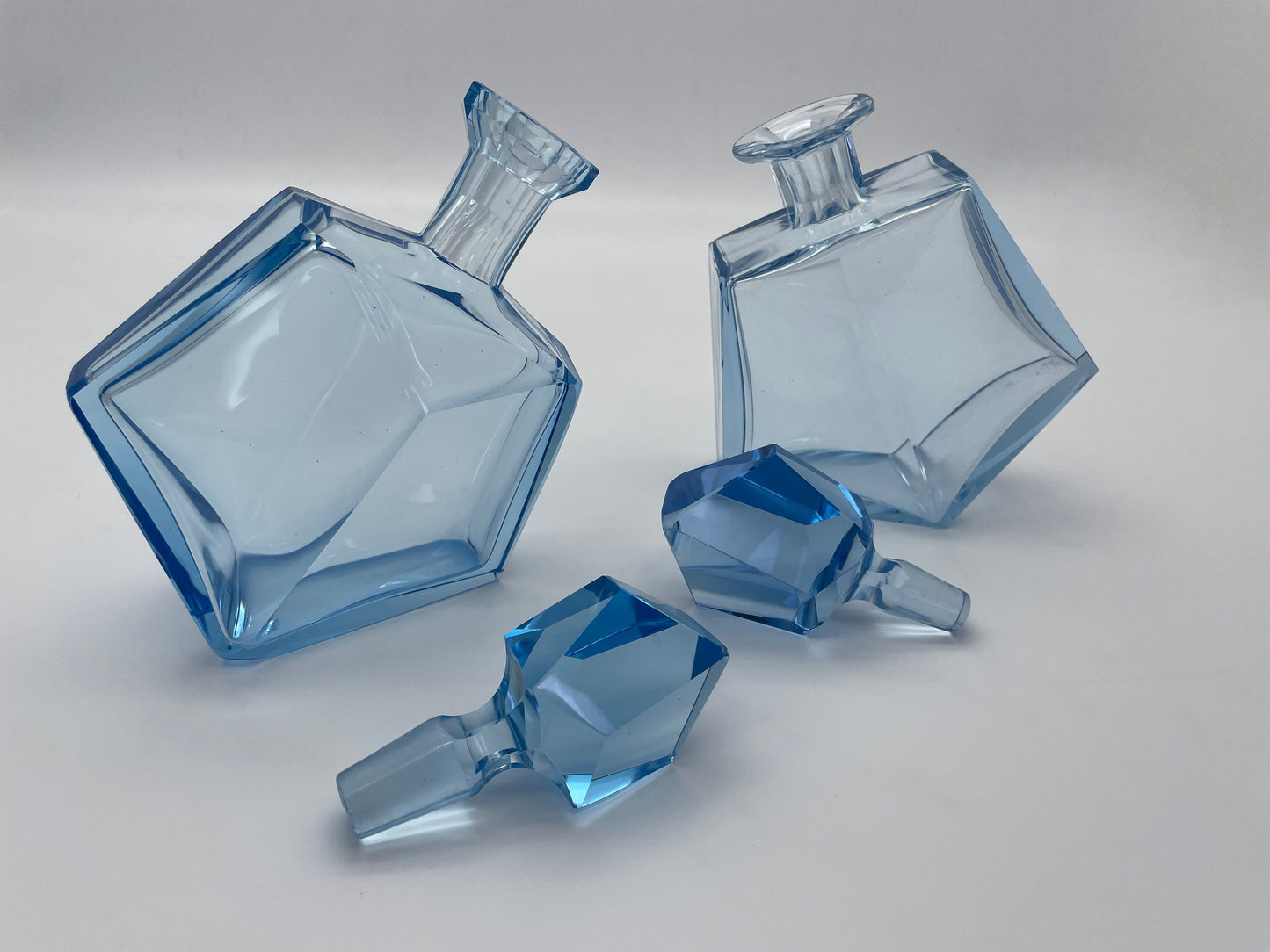 Pair of vintage blue glass decanters displayed with removable faceted glass stoppers beside the bottles.