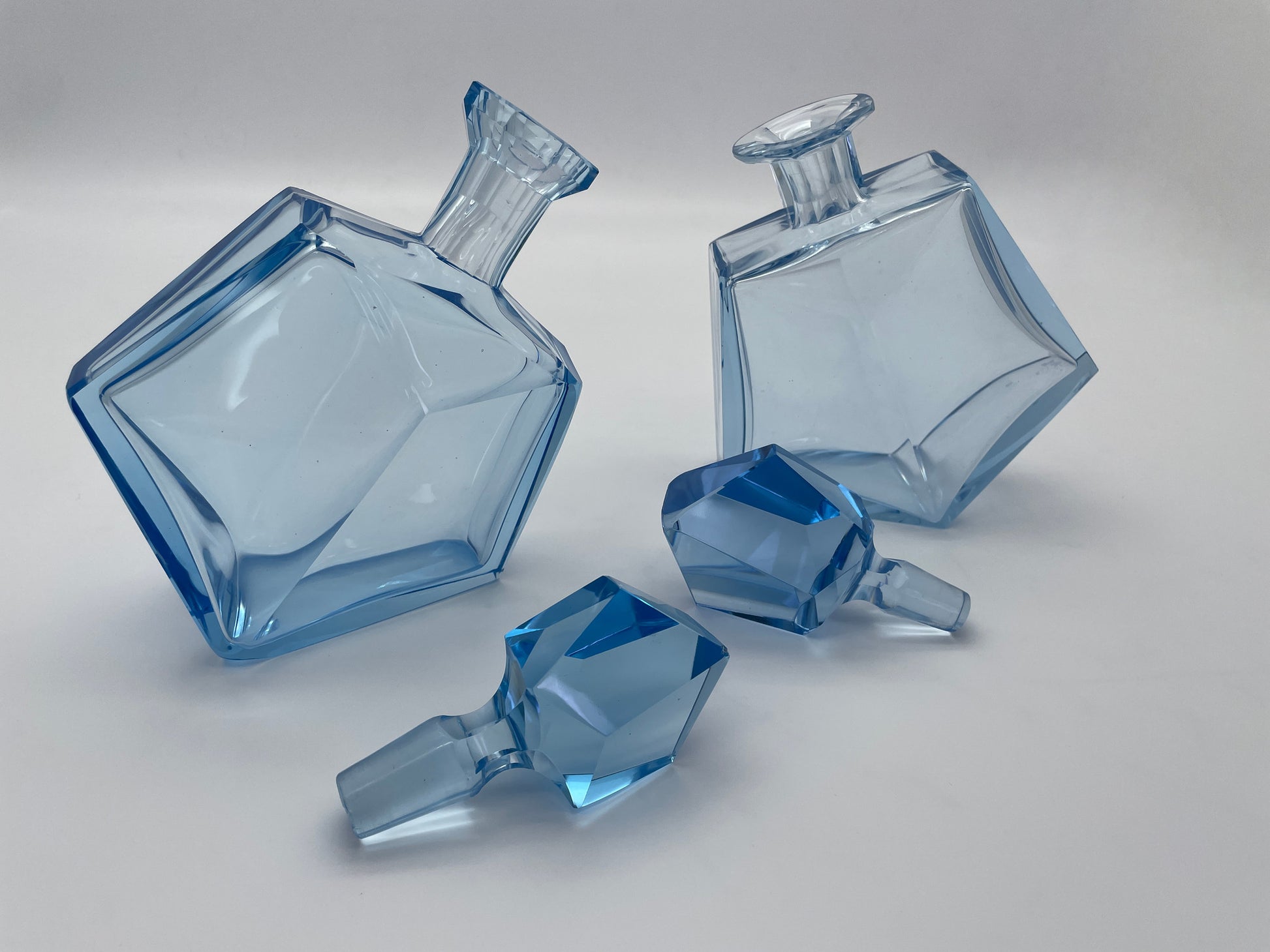 Pair of vintage blue glass decanters displayed with removable faceted glass stoppers beside the bottles.