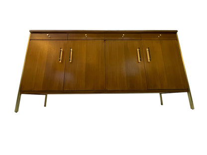 Low angle front view of a restored Paul McCobb for Calvin Group ribbon mahogany credenza with four drawers, four doors, brass hardware, and brass post legs.