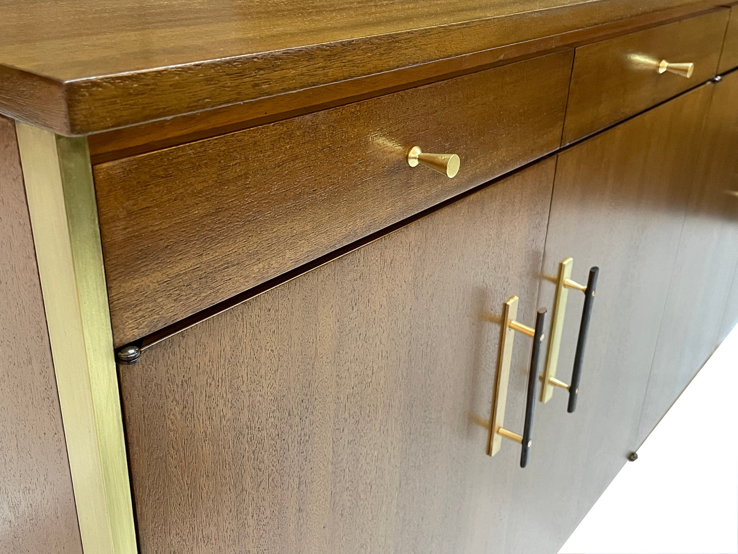 Detail view of ribbon mahogany grain, brass drawer pull, and brass-trimmed case on a restored Paul McCobb Calvin Group credenza from the 1960s.
