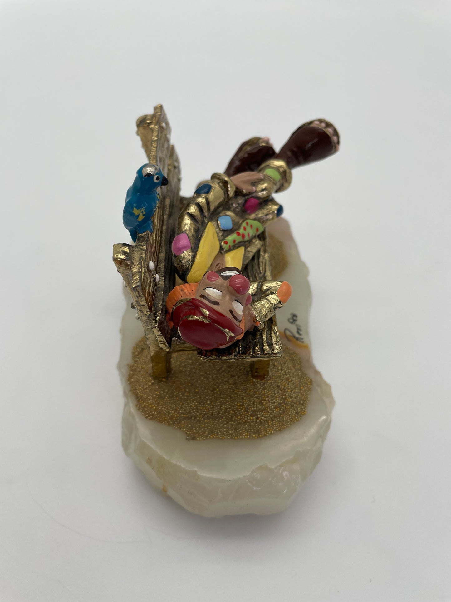 Side view of a vintage Ron Lee clown figurine resting on a park bench with a blue bird, hand-painted details, oversized clown shoes, and natural onyx base.