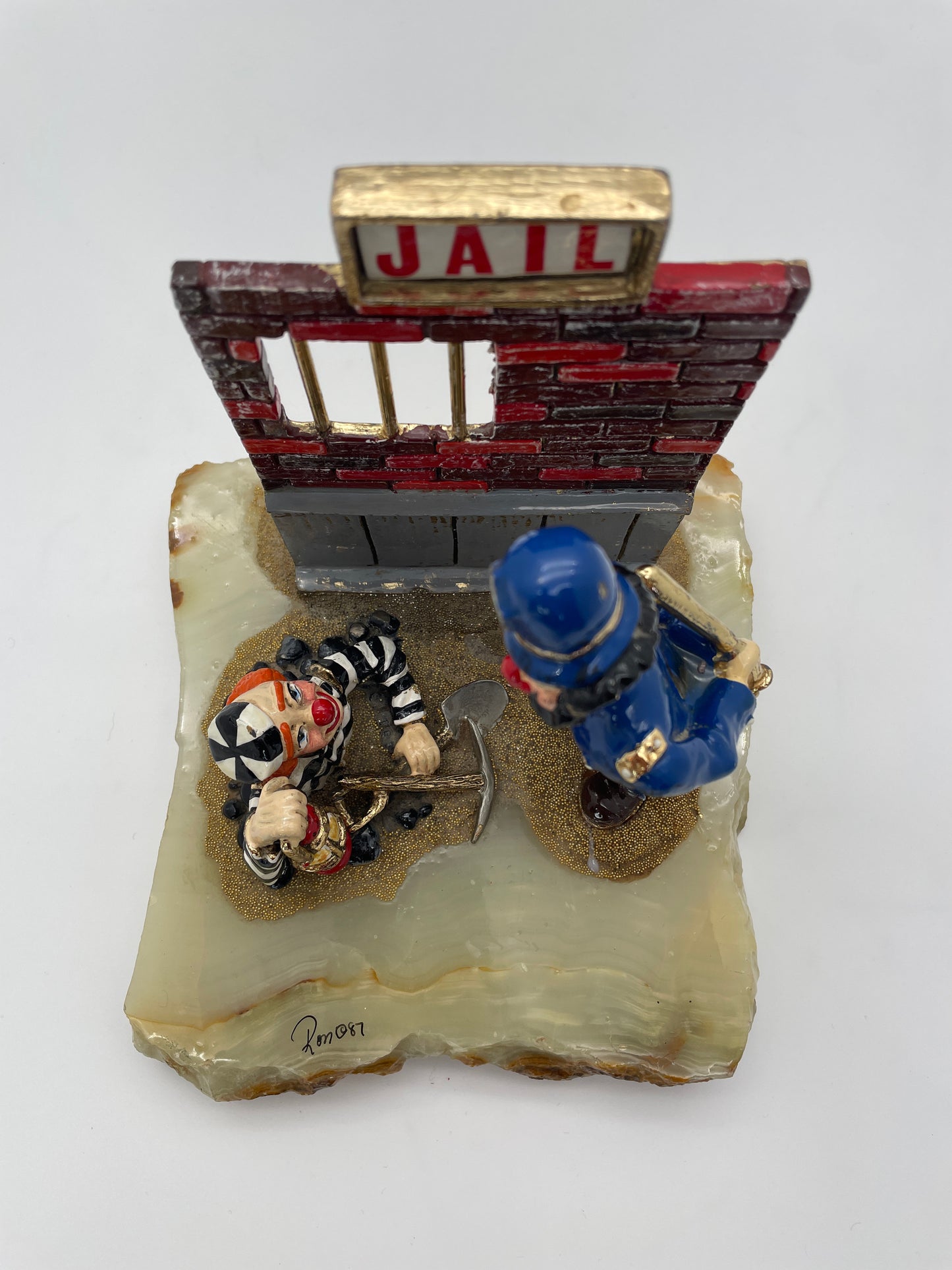 Overhead view of Ron Lee Great Escape clown sculpture showing the jail wall, prisoner clown, police officer, lantern, pickaxe, and natural onyx base.