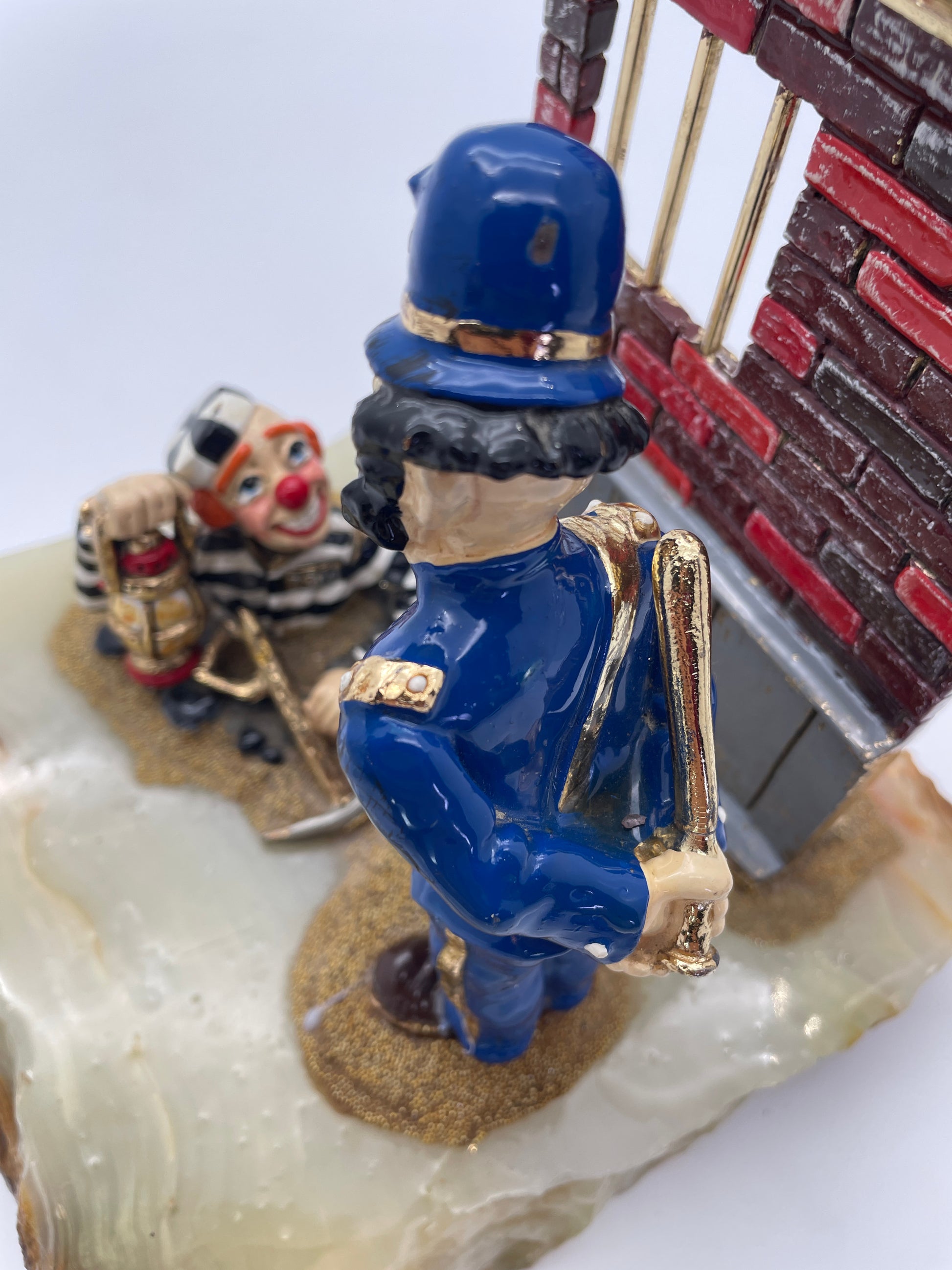 Over-the-shoulder view of the police clown watching the prisoner in Ron Lee’s Great Escape sculpture on a natural onyx base.