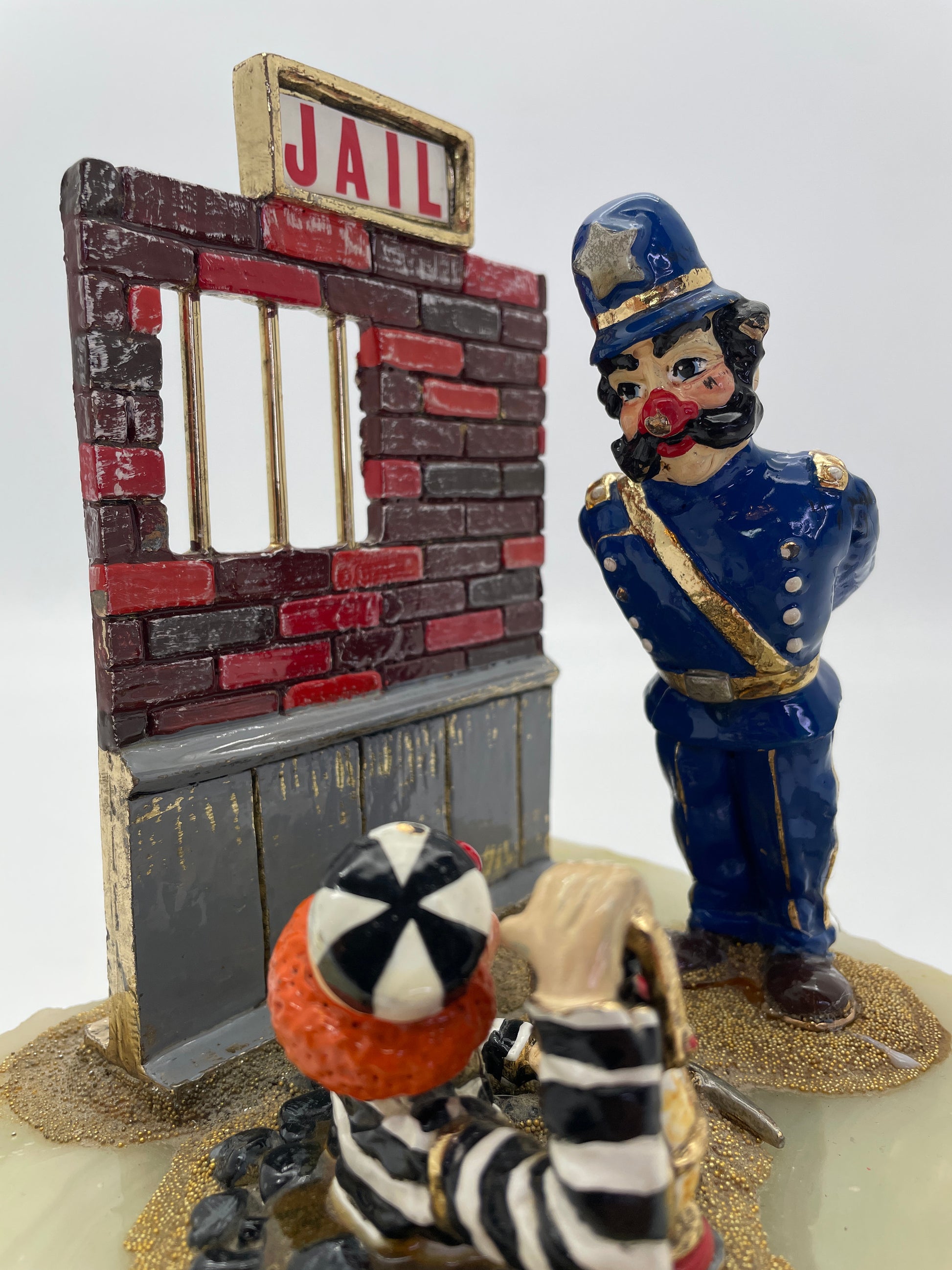 Close-up of Ron Lee Great Escape clown sculpture showing the police officer confronting a prisoner clown escaping beneath a jail wall with hand-painted details and 24K gold-plated accents.