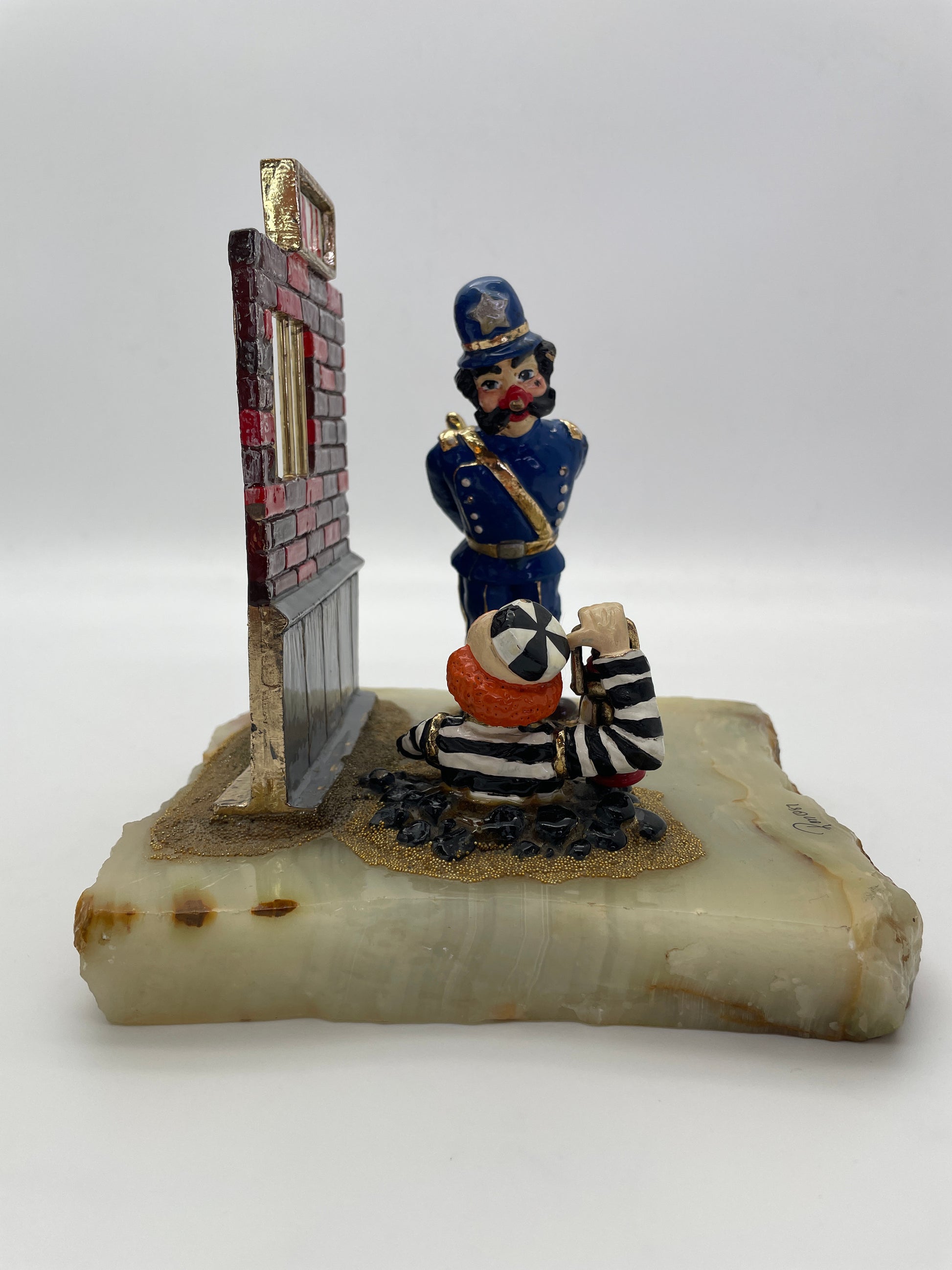 Left side profile of Ron Lee Great Escape clown sculpture featuring a prisoner clown emerging from a tunnel while a police officer stands watch beside the jail wall.