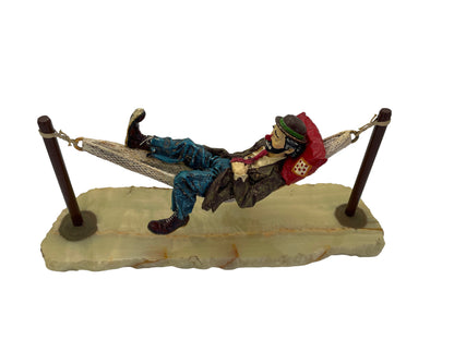Top angled view of a signed Ron Lee hand-painted pewter hobo clown sculpture resting in a hammock on an onyx base.