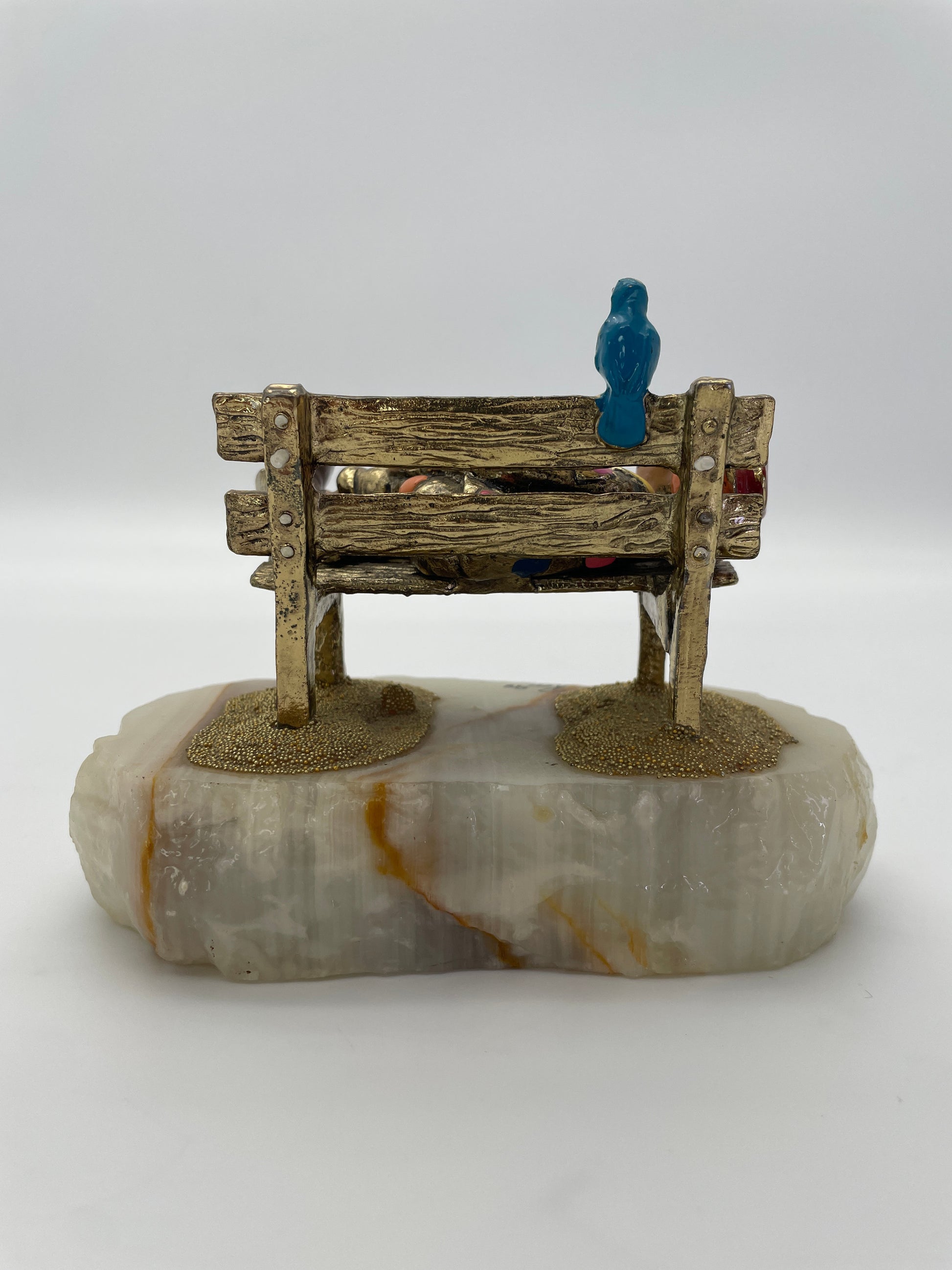 Rear view of a vintage Ron Lee sleeping clown sculpture on a rustic park bench with blue bird, 24K gold-plated finish, and natural banded onyx base.