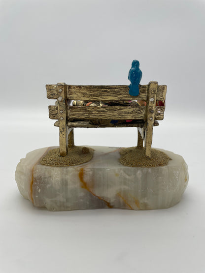 Rear view of a vintage Ron Lee sleeping clown sculpture on a rustic park bench with blue bird, 24K gold-plated finish, and natural banded onyx base.