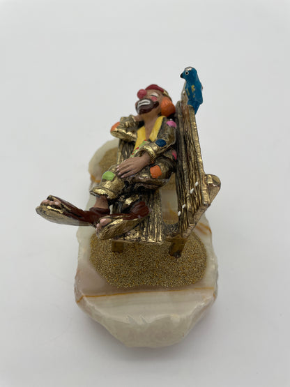 Angled view of a signed Ron Lee sleeping clown circus figurine featuring a textured park bench, blue bird, 24K gold-plated finish, and natural onyx base.