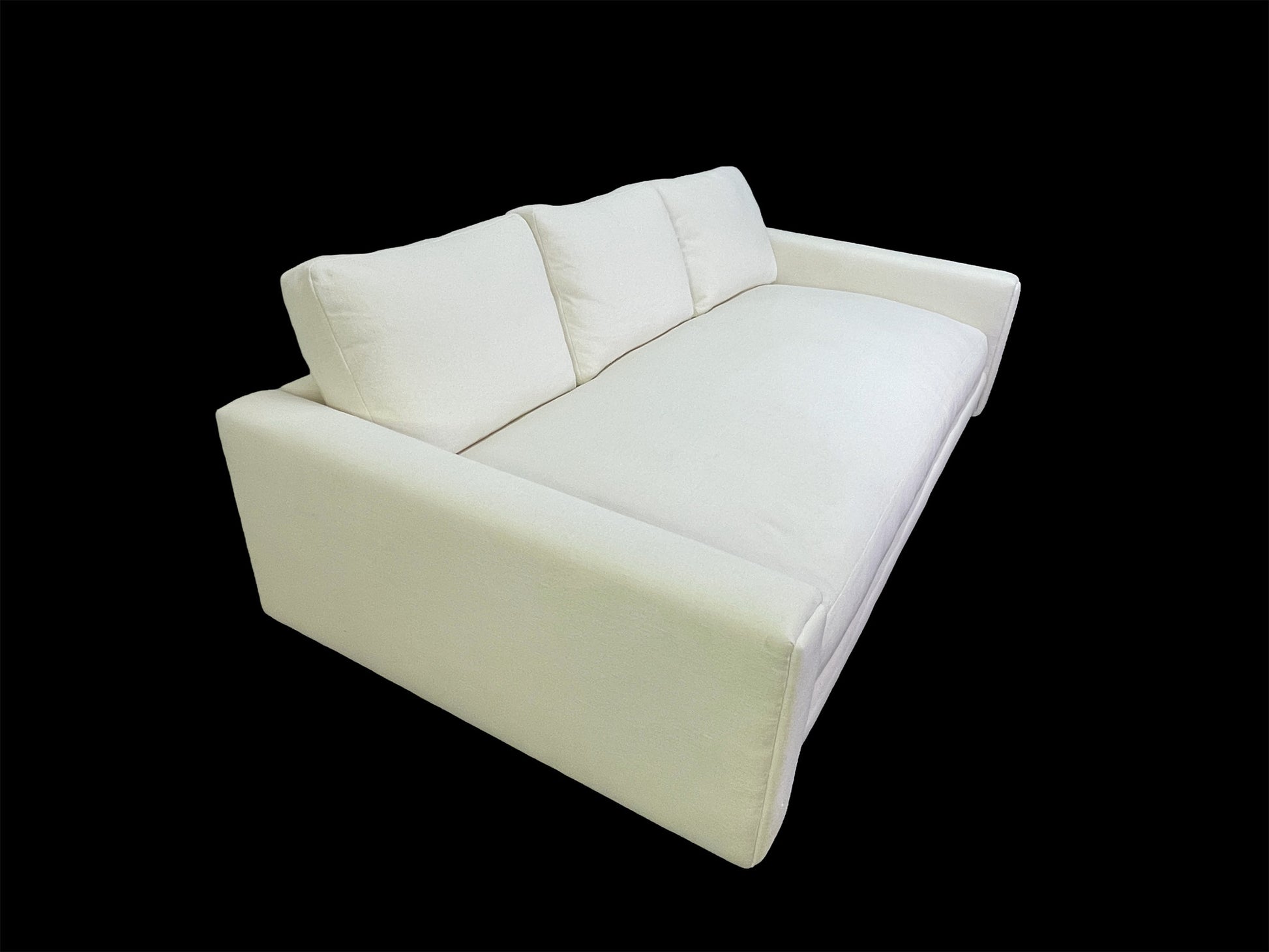 Three-quarter view of custom luxury white upholstered daybed with deep seat cushion and sculptural lines black background.