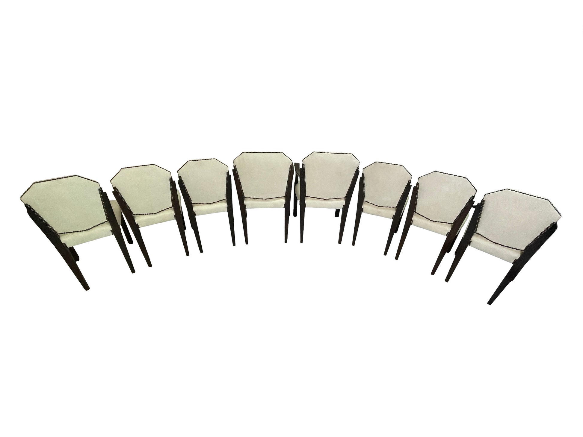 Rear angled view of a vintage set of 8 Art Deco style dining chairs with ivory upholstery, dark mahogany frames, and nailhead trim.