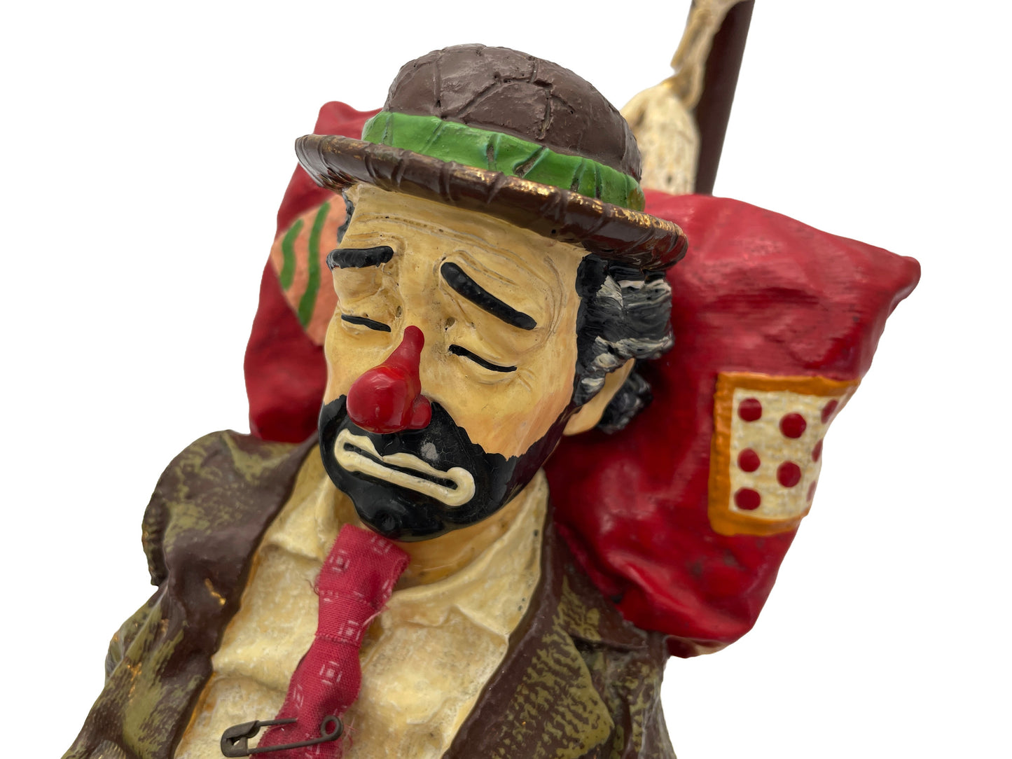 Close-up of the expressive hand-painted face of a signed Ron Lee hobo clown sculpture with a red pillow and natural onyx base.