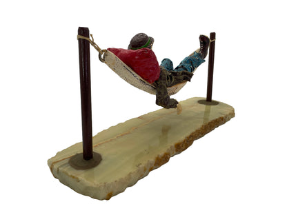 Rear three-quarter view of a signed 1988 Ron Lee hobo clown sculpture resting in a hammock on a natural onyx base.