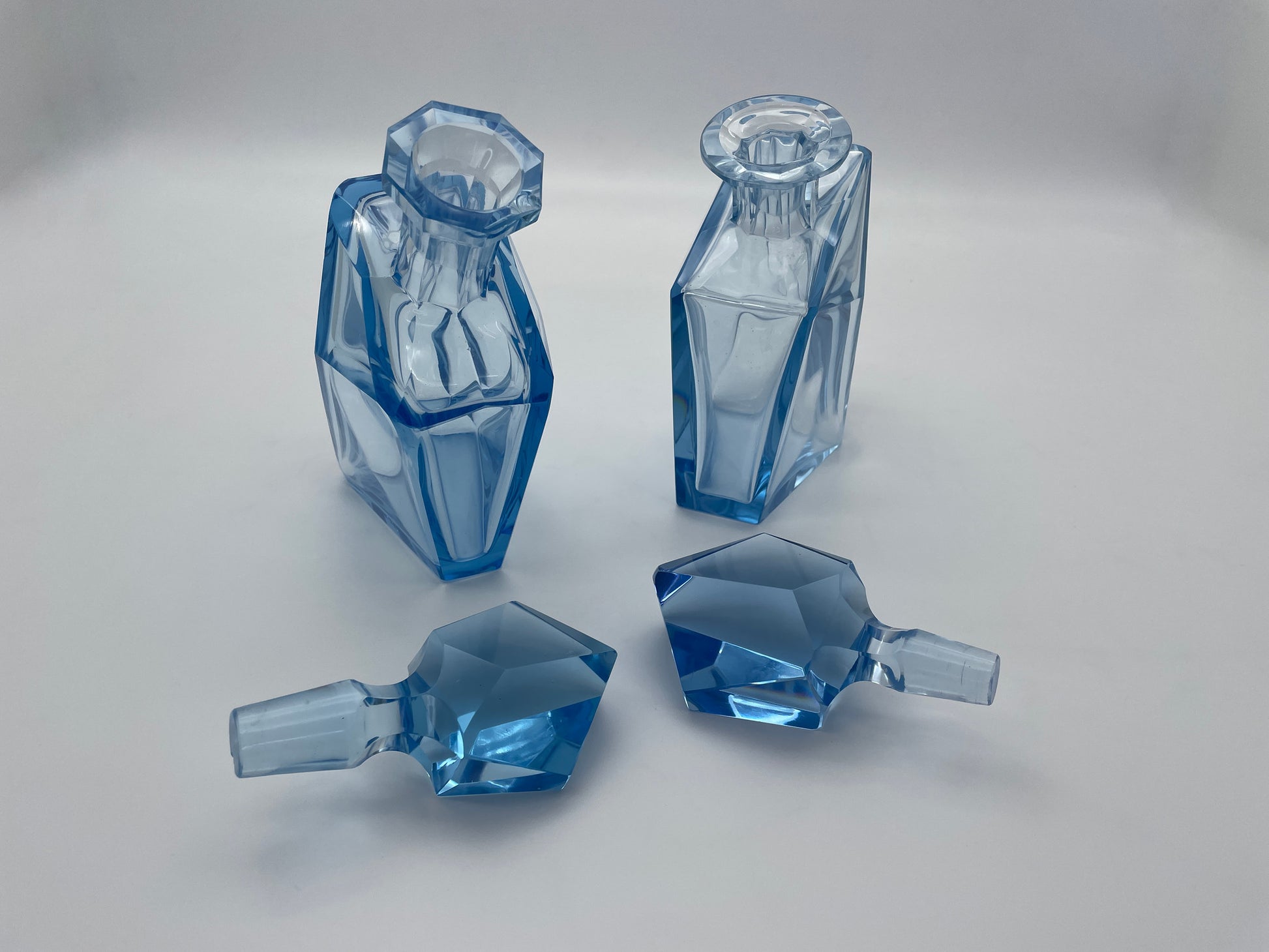 Pair of vintage blue glass decanters with faceted glass stoppers removed and displayed alongside the bottles.