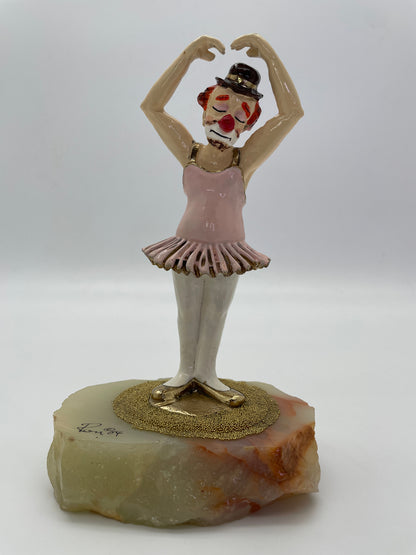 Angled front view of a vintage Ron Lee ballet clown sculpture wearing a pink tutu on a natural onyx base.