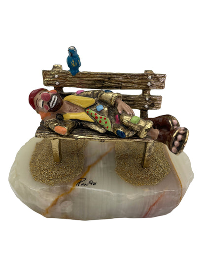 Vintage Ron Lee sleeping clown sculpture resting on a park bench with a blue bird, hand-painted with 24K gold-plated finish on a natural onyx base, signed 1988.